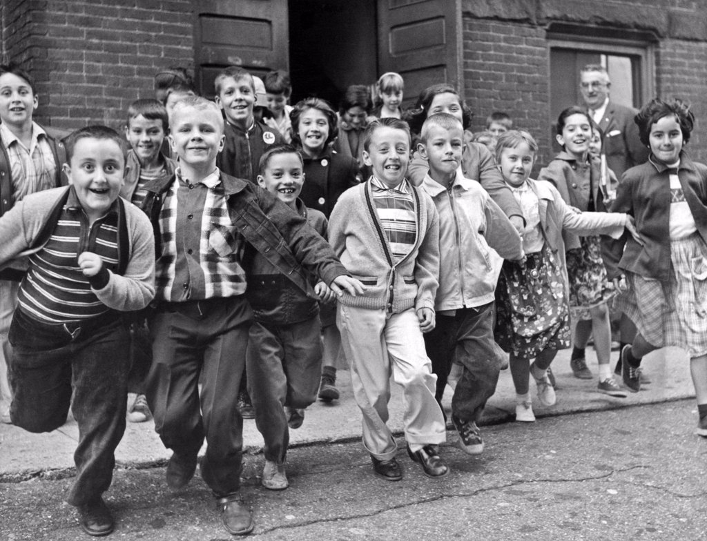 STUDENTS RUSHING OUT OF THE SCHOOL BUILDING FOR SUMMER VACATION ON THE LAST DAY OF CLASSES.