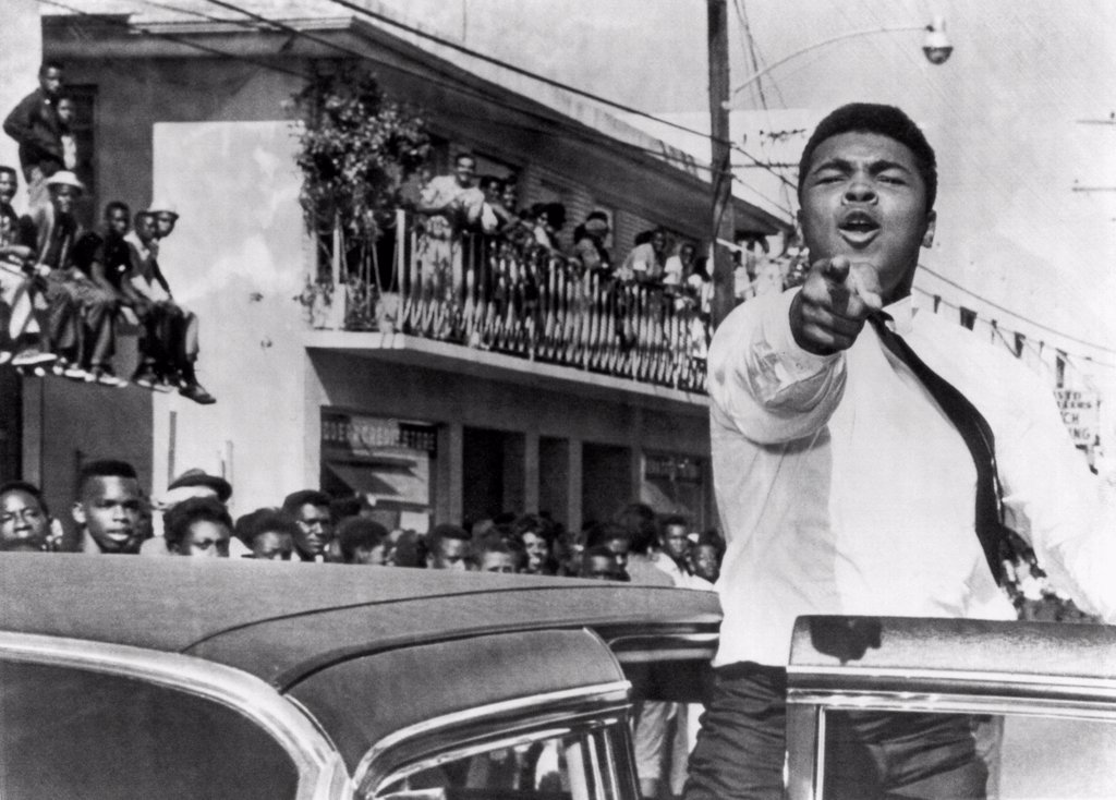 CASSIUS CLAY WHO IS TRAINING IN MIAMI FOR HIS TITLE FIGHT AGAINST SONNY LISTON, TAKES PART IN A PRE FOOTBALL GAME PARADE.