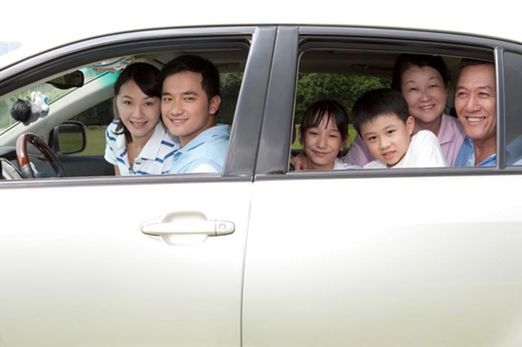 MULTI-GENERATIONAL FAMILY SITTING IN CAR AND LOOKING OUT THROUGH CAR WINDOWS, SMILING