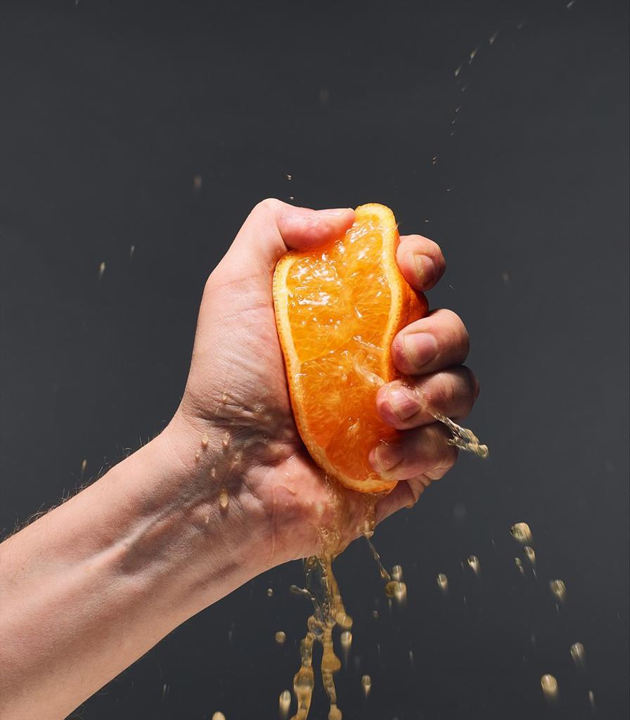 MALE HAND SQUEEZING JUICY ORANGE, DARK BACKGROUND