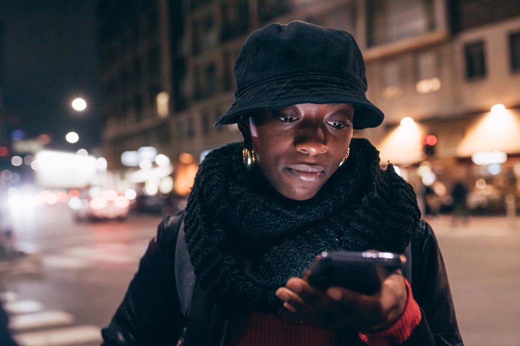 WOMAN LOOKING AT SMART PHONE IN CITY AT NIGHT