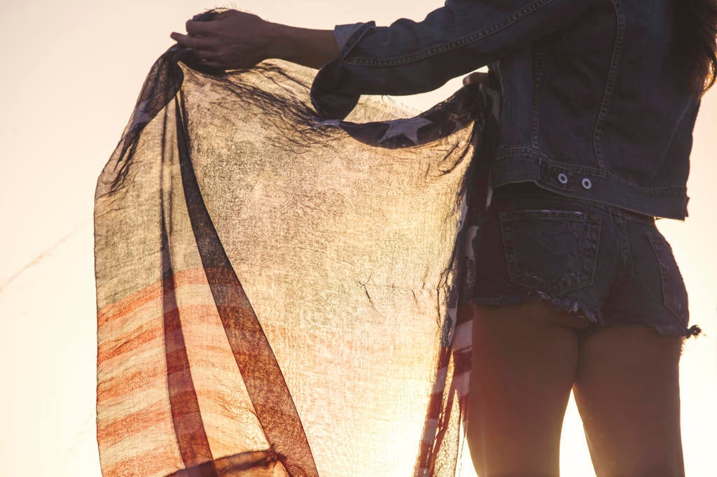 Woman wearing denim shorts, holding American flag, mid section, rear view