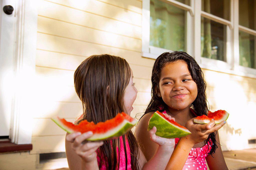 TWO SMILING GIRLS SITTING ON HOUSE PORCH WITH SLICES OF WATERMELON