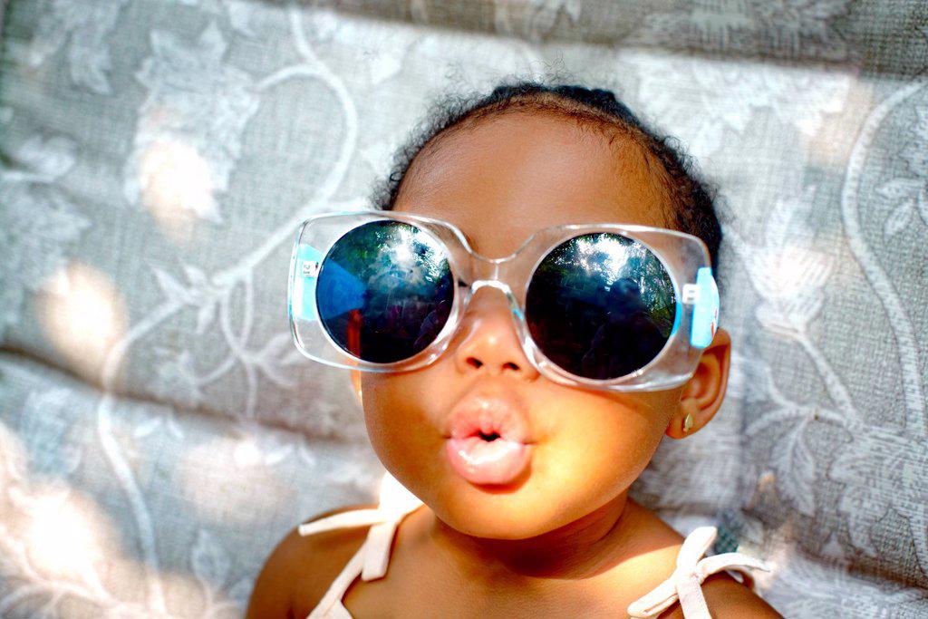 BABY GIRL SITTING ON LOUNGE CHAIR WEARING SUNGLASSES