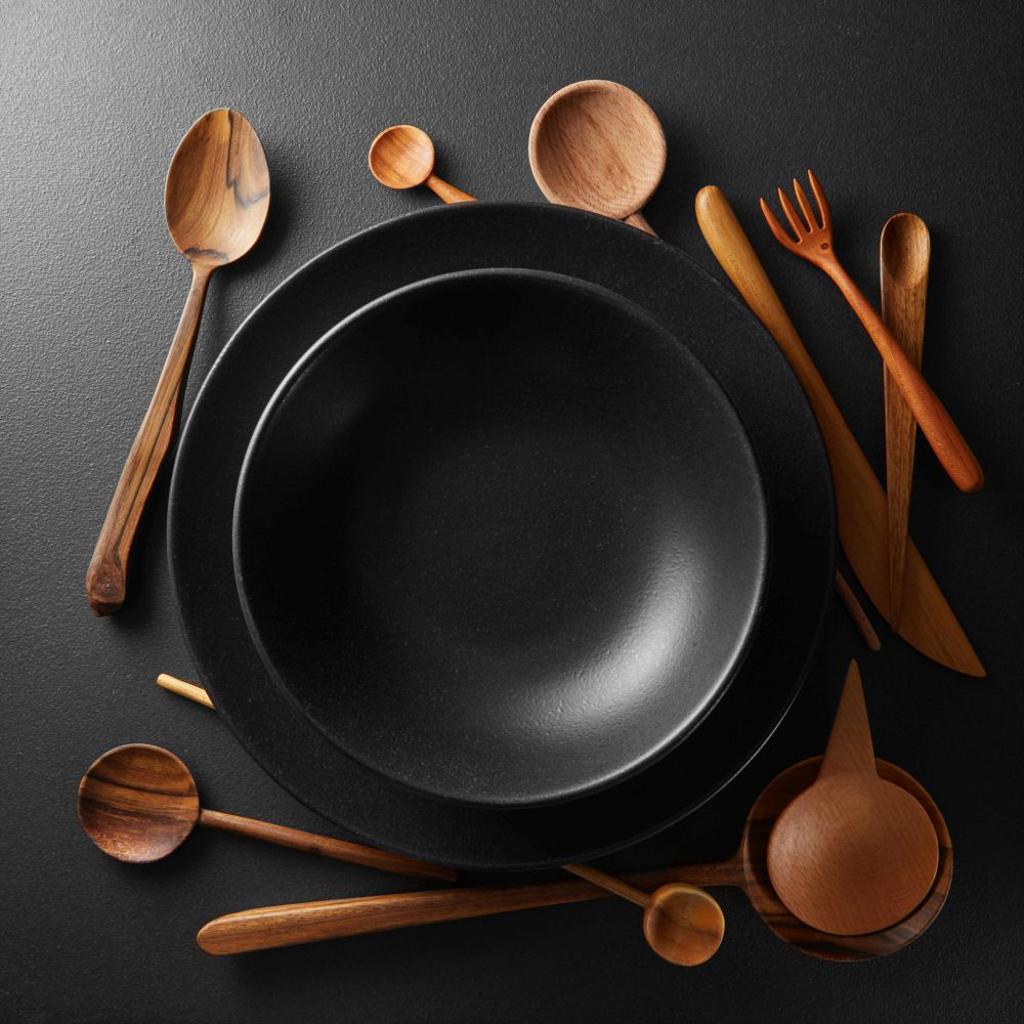 BLACK PLATES AND WOODEN SPOON, FORK, KNIFE ON A BLACK TABLE. PLATES AND WOODEN CUTLERY