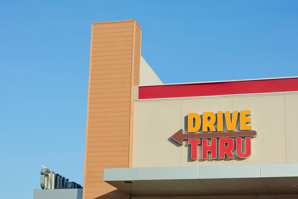 DRIVE THRU SIGN WITH LEFT ARROW ON BUILDING AGAINST THE BLUE CLEAR SKY