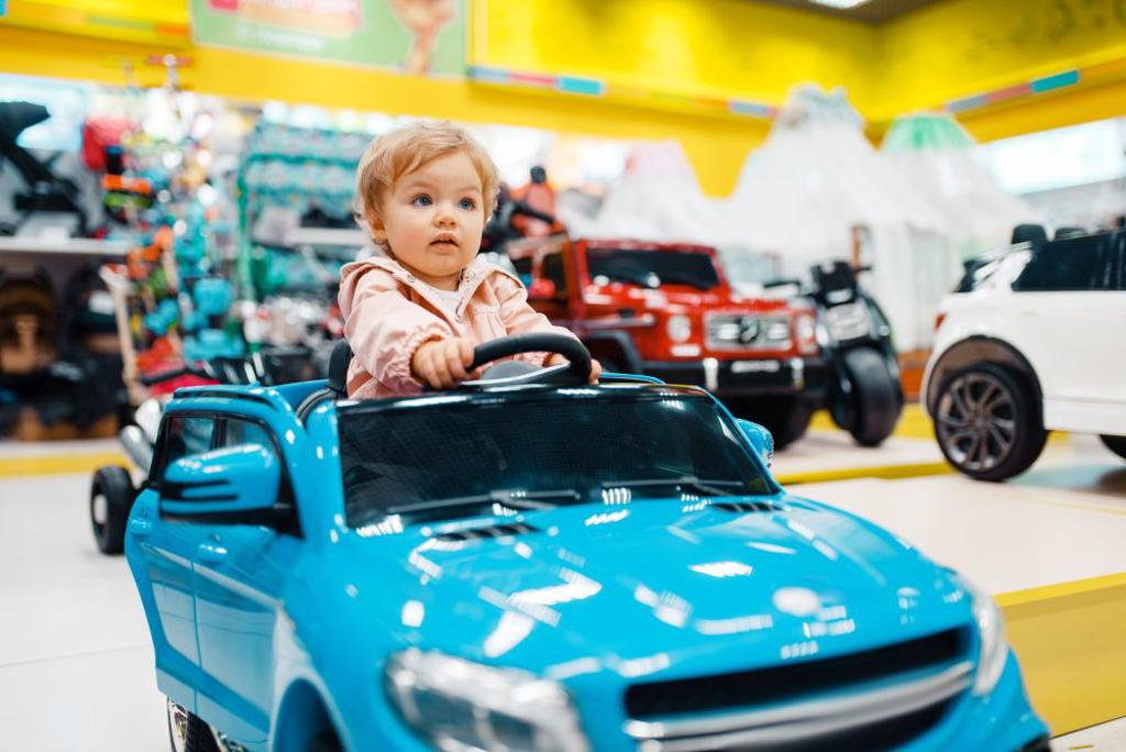 LITTLE GIRL CHOOSING ELECTROMOBILE IN KIDS STORE