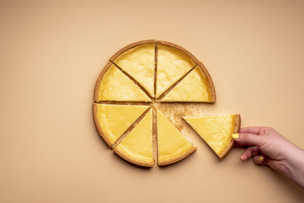 WOMAN'S HAND GRABBING A PIECE OF CHEESECAKE. SLICED CHEESE TART ON A YELLOWISH BACKGROUND