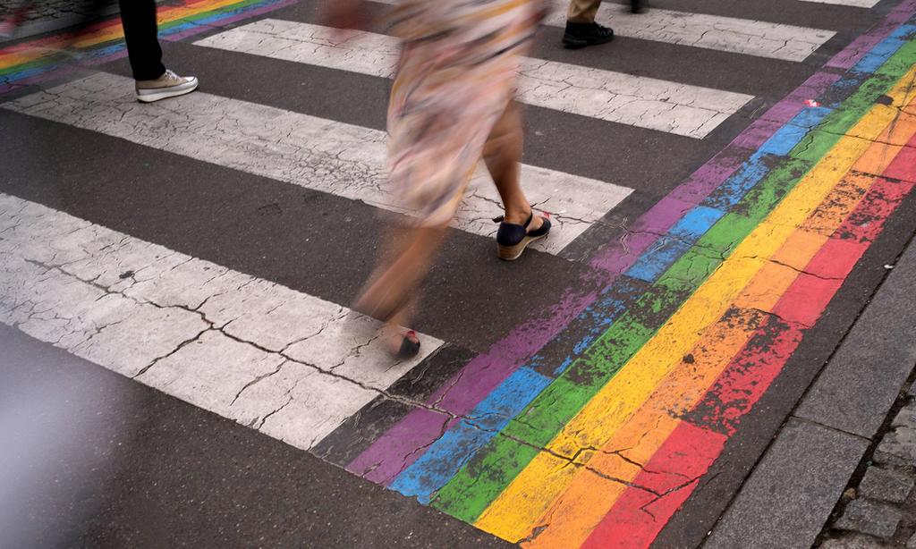 Blurred feet of woman crossing a rainbow accented crosswalk.