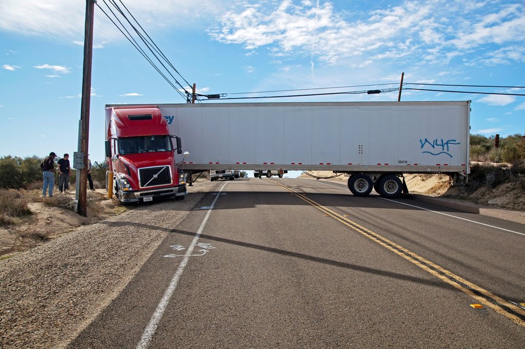 A TRACTOR-TRAILER IS STUCK IN SOFT SAND AND WEDGED BETWEEN UTILITY EQUIPMENT, BLOCKING TRAFFIC ON CALIFORNIA HIGHWAY 94