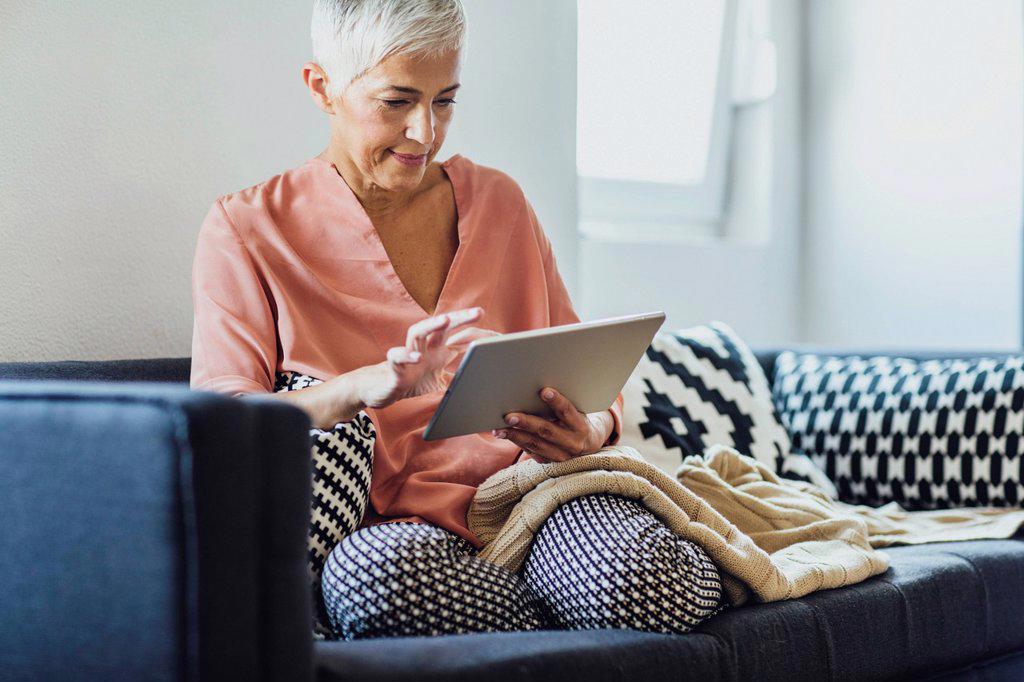 OLDER CAUCASIAN WOMAN USING DIGITAL TABLET ON SOFA