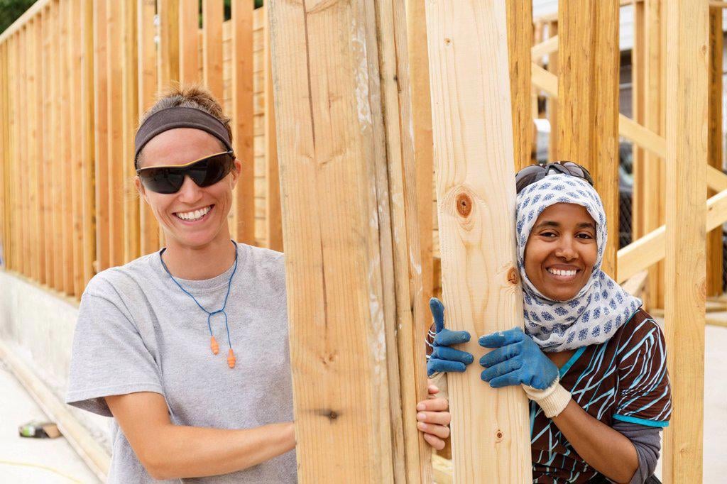 SMILING VOLUNTEERS HOLDING LUMBER AT CONSTRUCTION SITE