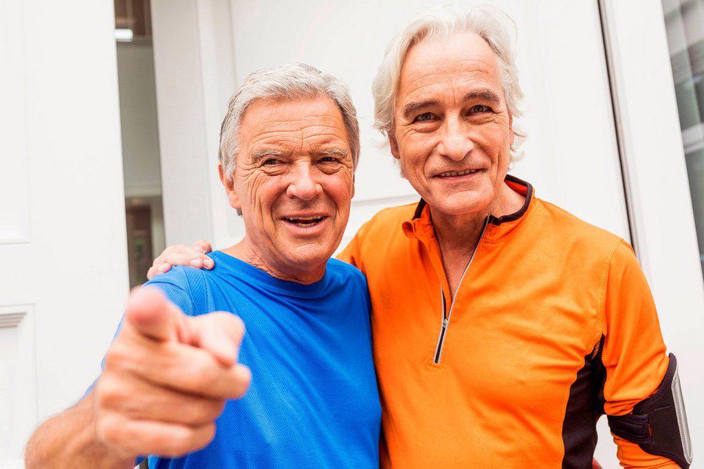 PORTRAIT OF TWO HAPPY SENIOR MALE RUNNERS AT FRONT DOOR