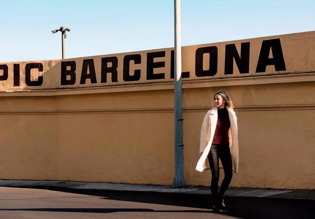 FEMALE TOURIST STROLLING BY WALL WITH BARCELONA IN CAPITAL LETTERS