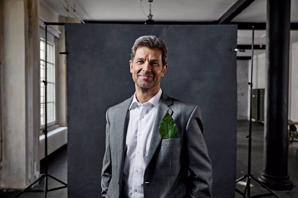 PORTRAIT OF MATURE BUSINESSMAN WITH LEAF IN POCKET IN FRONT OF BLACK BACKDROP IN LOFT