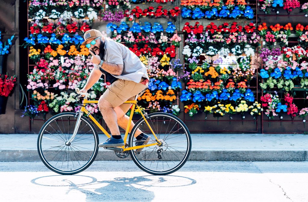 PORTRAIT OF BEARDED MAN ON FIXIE BIKE STICKING OUT TONGUE AND SHOWING ROCK AND ROLL SIGN