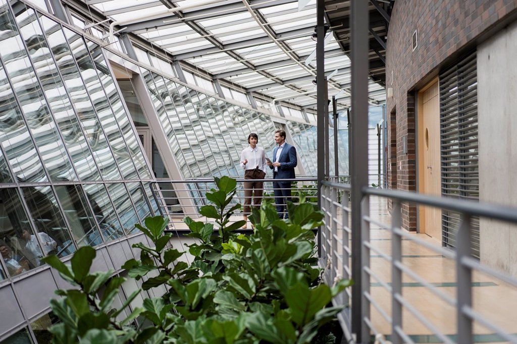 BUSINESSMAN AND WOMAN TALKING IN SUSTAINABLE OFFICE BUILDING, USING DIGITAL TABLET