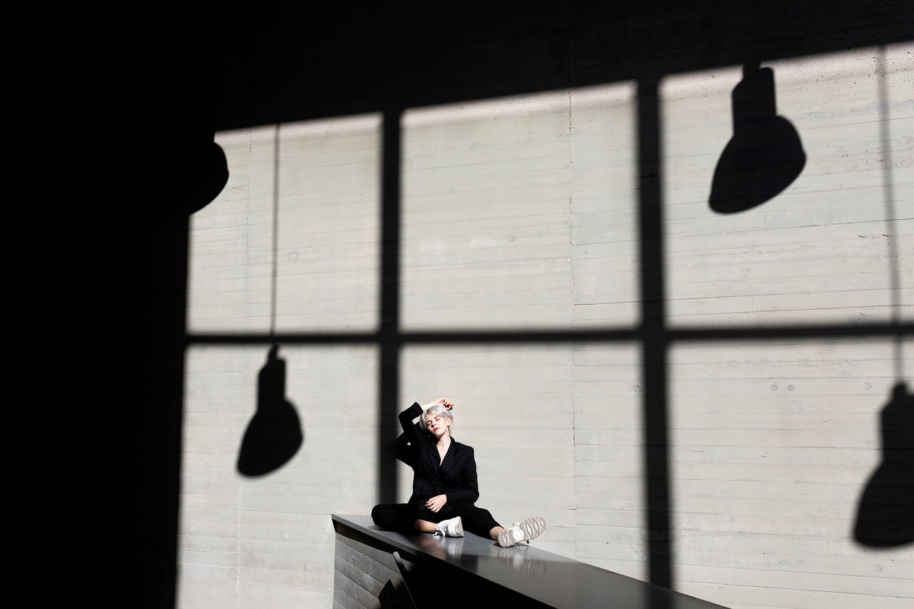 FEMALE PROFESSIONAL WEARING ELEGANT SUIT RELAXING ON RETAINING WALL WITH SUNLIGHT AND SHADOW IN BACKGROUND