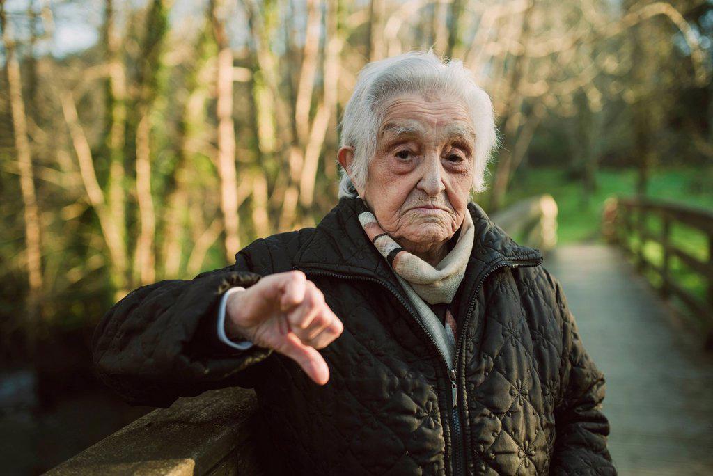 DISPLEASED SENIOR WOMAN SHOWING THUMBS DOWN GESTURE DURING WINTER