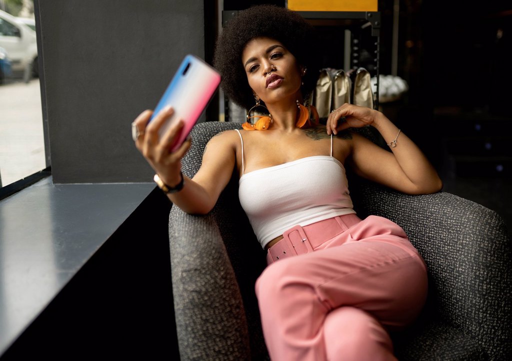 YOUNG WOMAN TAKING SELFIE ON SMART PHONE WHILE SITTING AT CAFE