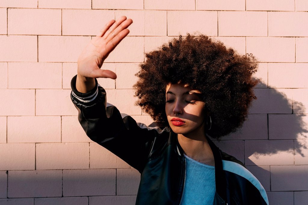 AFRO HAIR YOUNG WOMAN STRETCHING HAND IN FRONT OF BRICK WALL