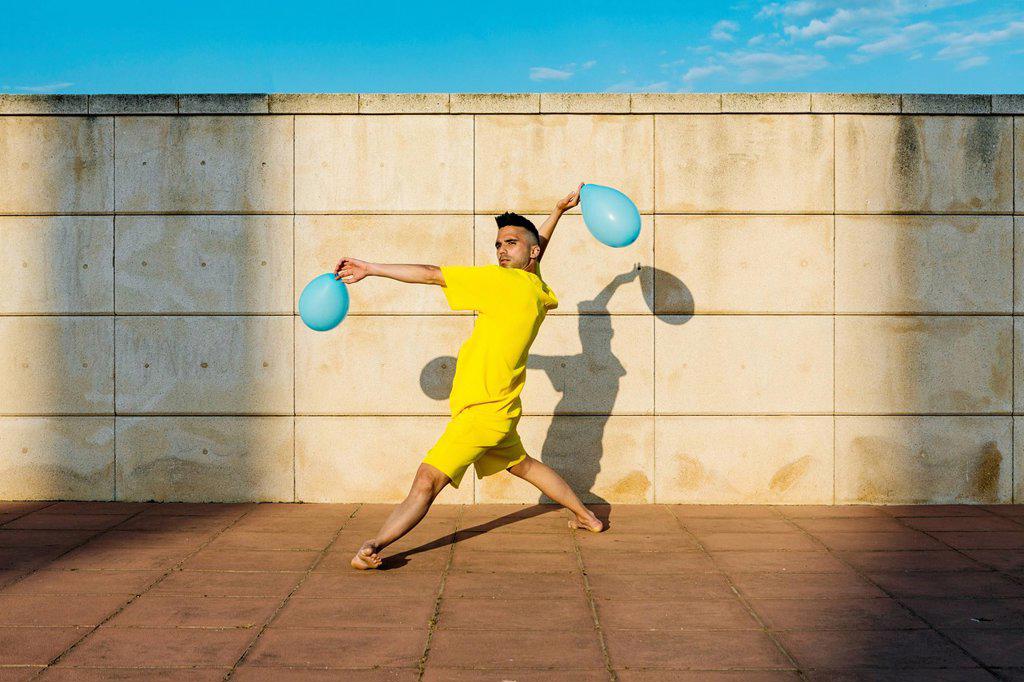 MAN DANCING WITH BALLOONS NEAR WALL DURING SUNNY DAY