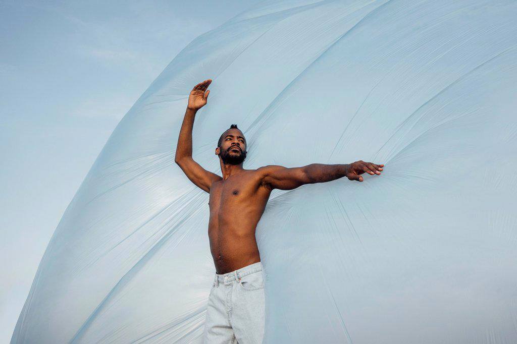 Shirtless man looking away while dancing in front of foil