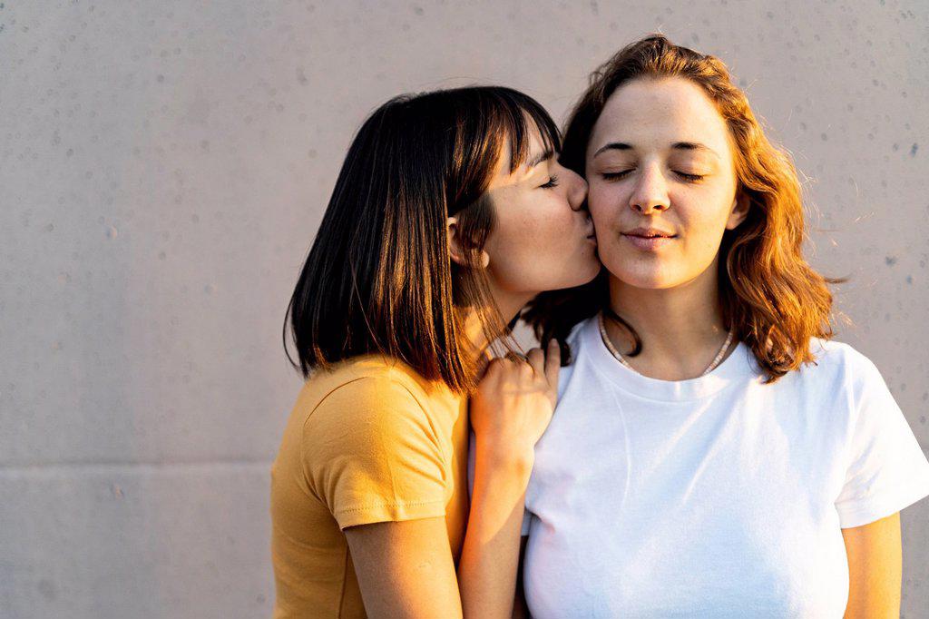 WOMAN WITH EYES CLOSED KISSING GIRLFRIEND IN FRONT OF WALL