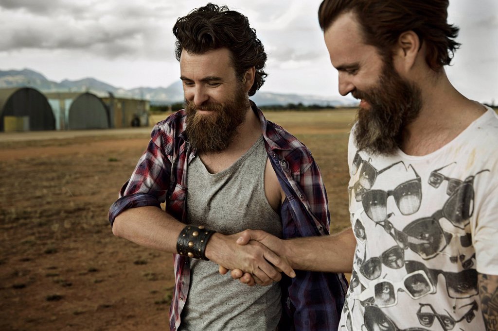 TWO MEN WITH FULL BEARDS IN ABANDONED LANDSCAPE SHAKING HANDS