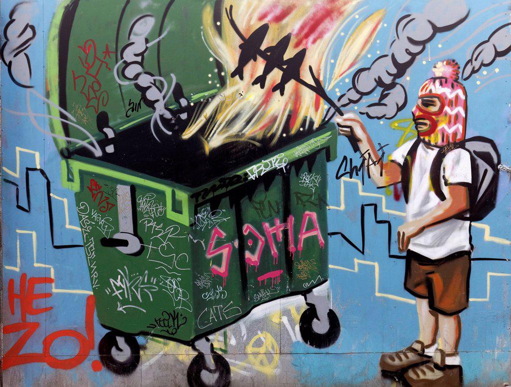 MAN WITH FACEMASK GRILLING FISH OVER A FIRE IN A DUMPSTER, MURAL, STREET ART
