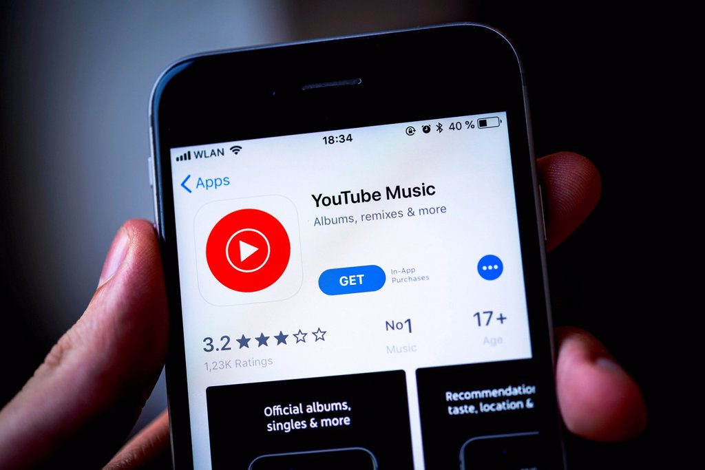 HAND HOLDING IPHONE WITH YOUTUBE MUSIC APP IN THE APPLE APP STORE