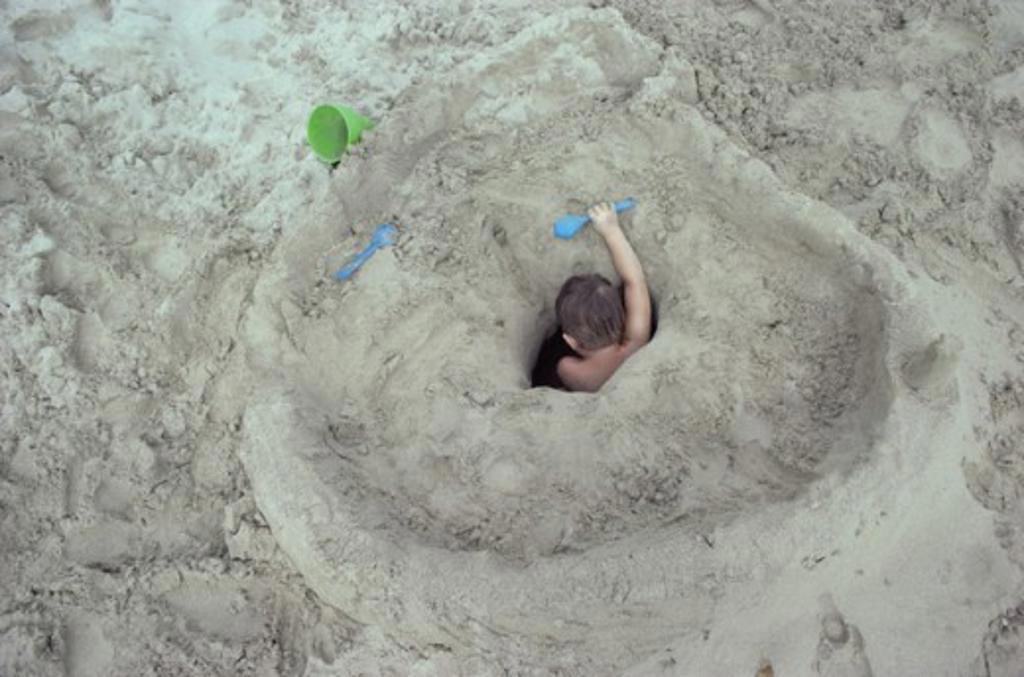 HIGH ANGLE VIEW OF A BOY DIGGING A HOLE ON THE BEACH