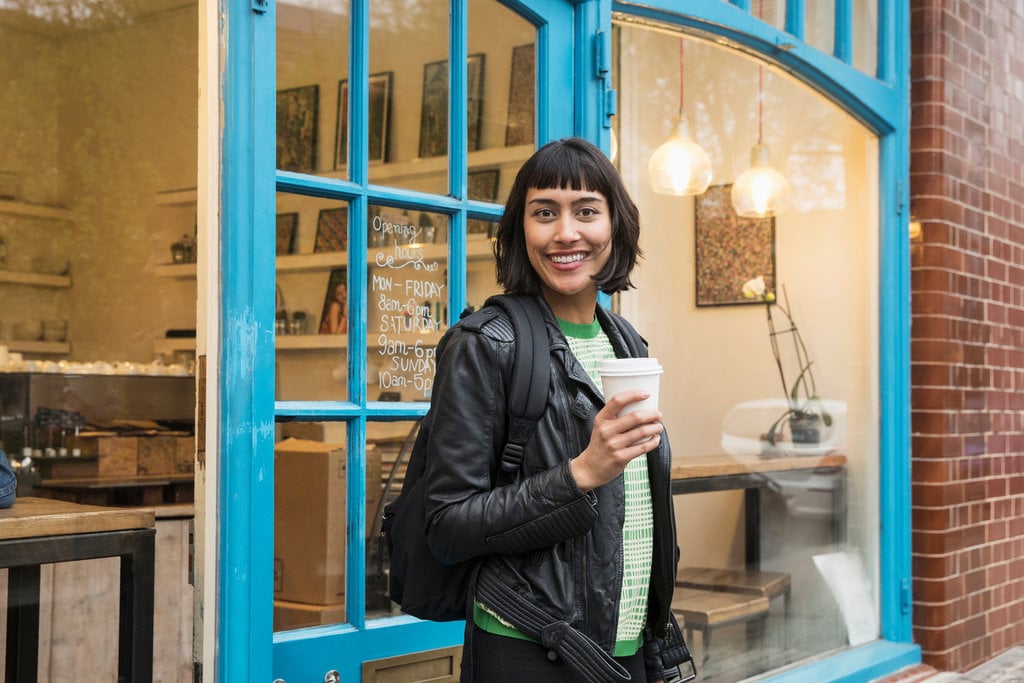 WOMAN WALKING OUT OF CAFE WITH COFFEE IN HAND
