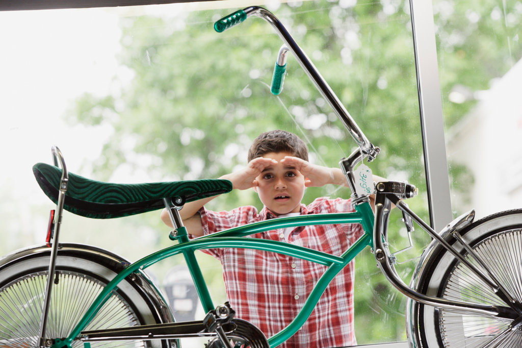 BOY LOOKING AT BIKE THROUGH STORE WINDOW