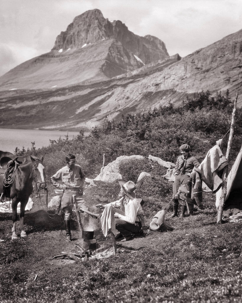 1920s THREE PEOPLE EASTERN VACATION COUPLE AND WESTERN COWBOY COOK AT CAMPSITE BY BAKER LAKE BANFF NATIONAL PARK ALBERTA CANADA