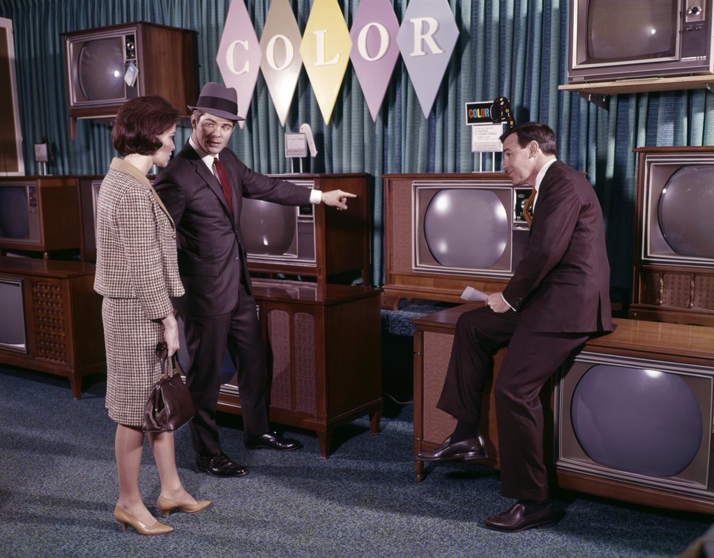 1960S COUPLE MAN WOMAN TALKING TO SALESMAN IN COLOR TELEVISION SET SALES DEPARTMENT