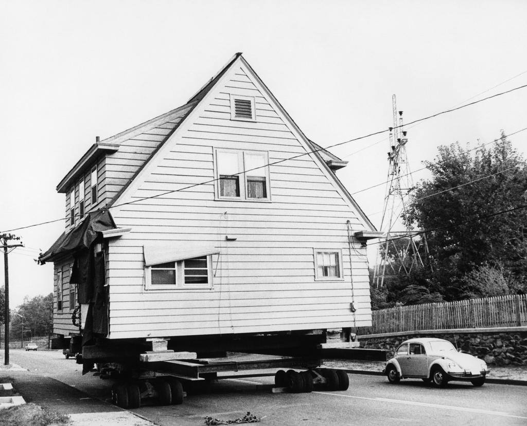 1970S Volkswagen Beetle Automobile Passing House Being Moved On Wheels Along Street