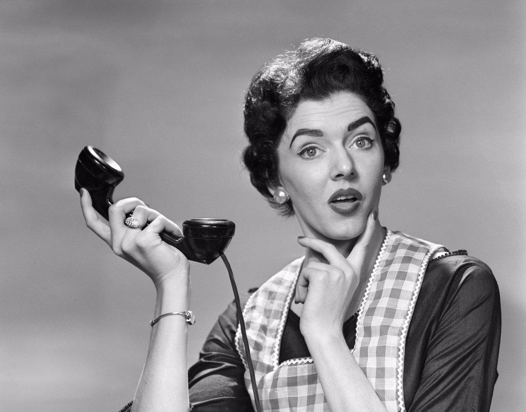 1950S CONFUSED WOMAN HOUSEWIFE HOLDING UP TELEPHONE RECEIVER