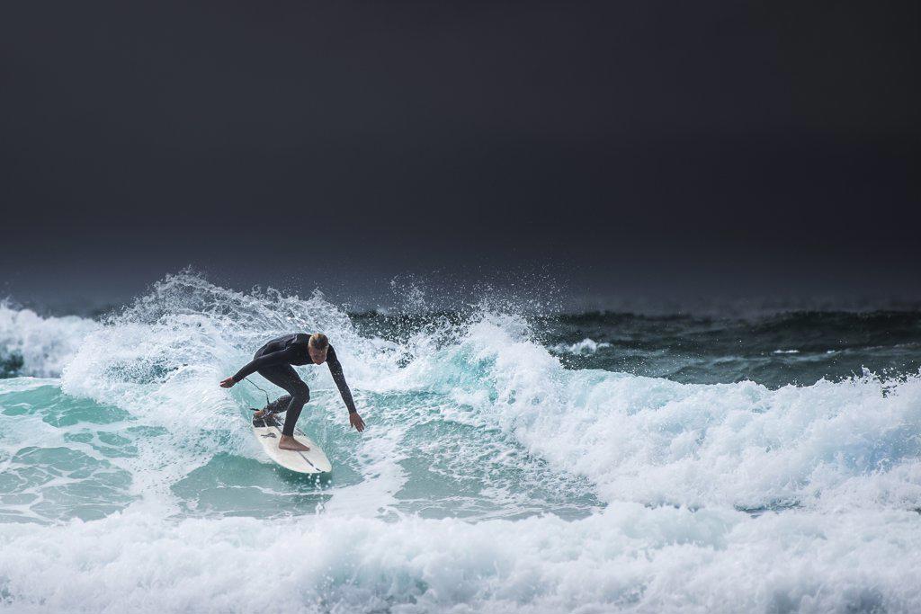 A LONE SURFER RIDING A WAVE AS DARK CLOUDS GATHER OVER THE NORTH CORNWALL COAST