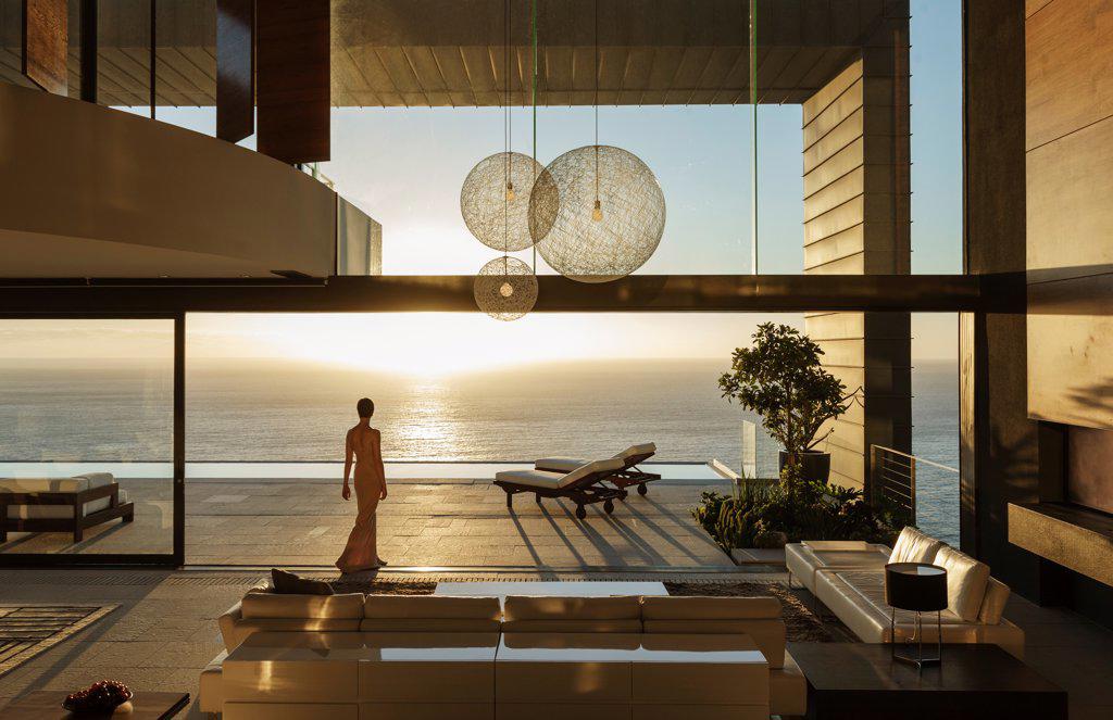 WOMAN IN MODERN HOUSE OVERLOOKING OCEAN