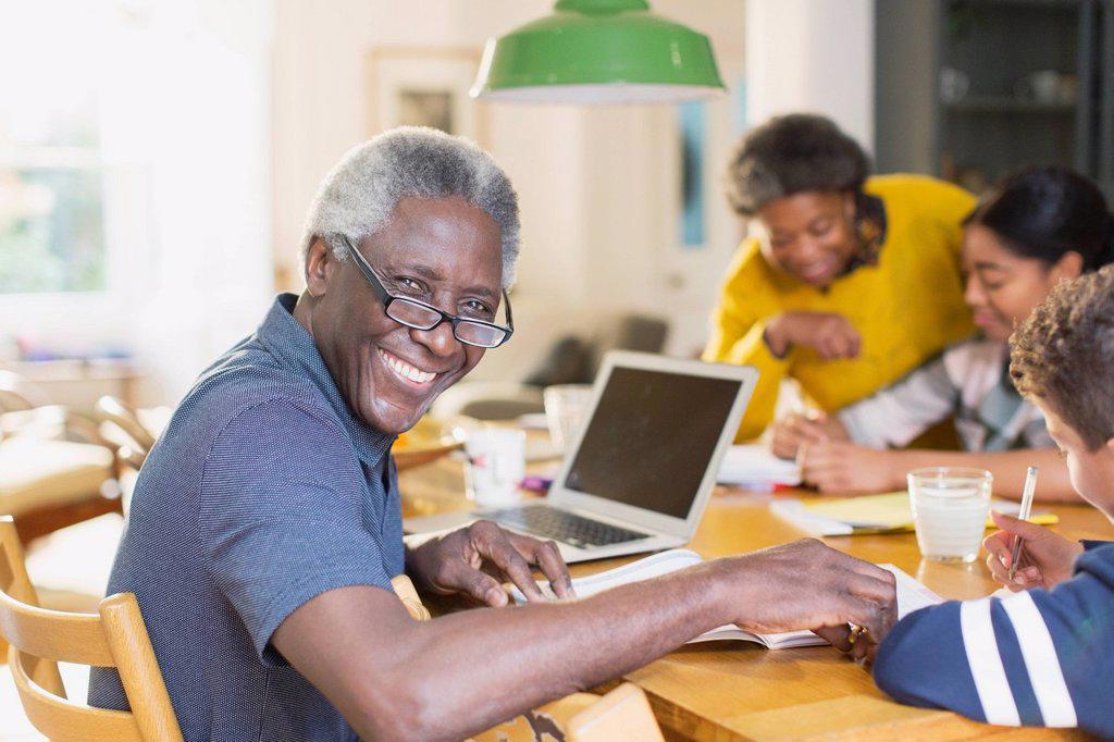 PORTRAIT SMILING, CONFIDENT SENIOR MAN USING LAPTOP WITH FAMILY