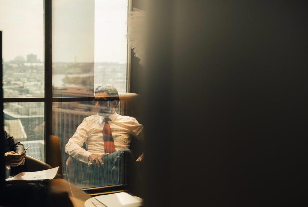 MATURE LAWYER SITTING WITH COLLEAGUE IN BOARD ROOM AT OFFICE