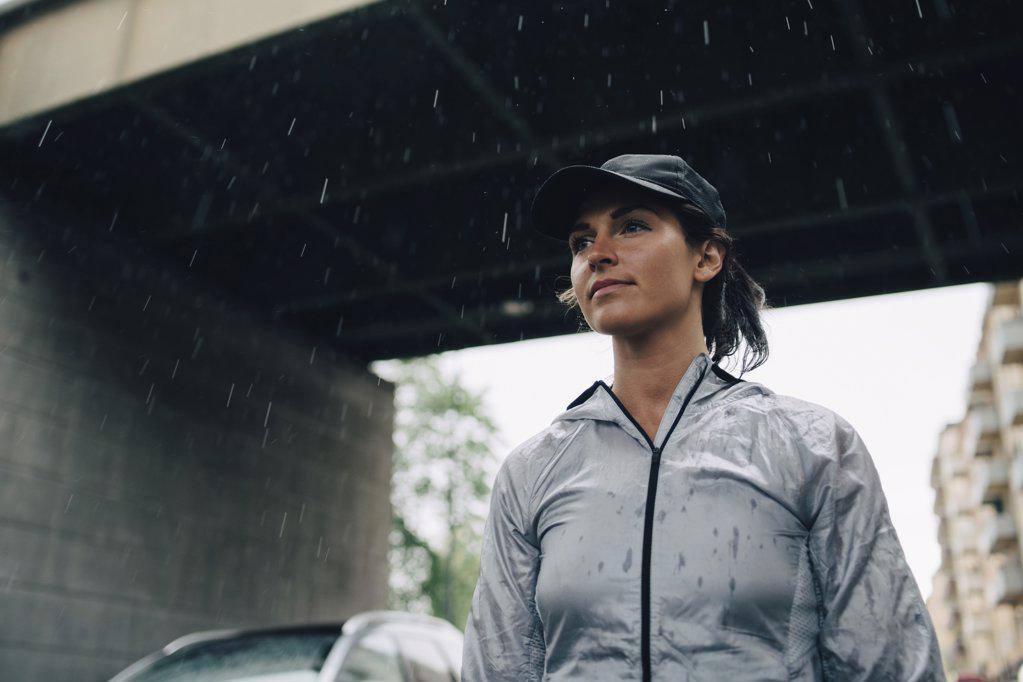 Low angle view of female athlete looking away while standing against bridge during rainy season