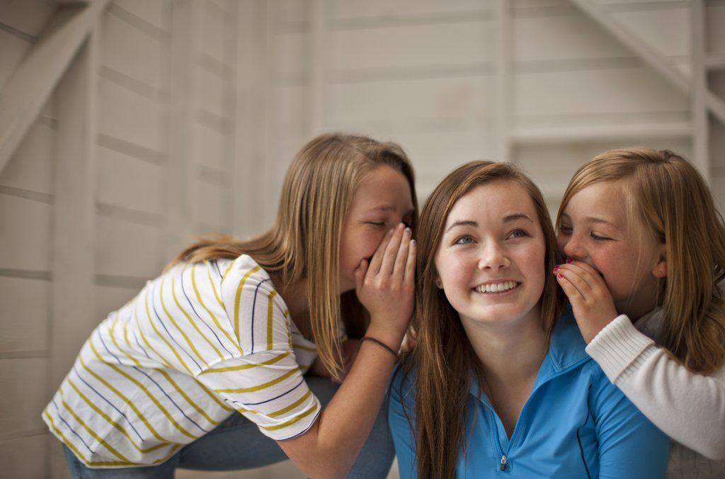 Grinning teenage girl listening while her two younger sisters whisper into both her ears