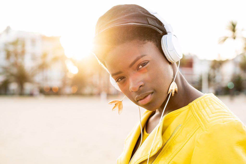 PORTRAIT OF AFRICAN AMERICAN WOMAN IN STYLISH BRIGHT JACKET LOOKING AT CAMERA ON SANDY BEACH