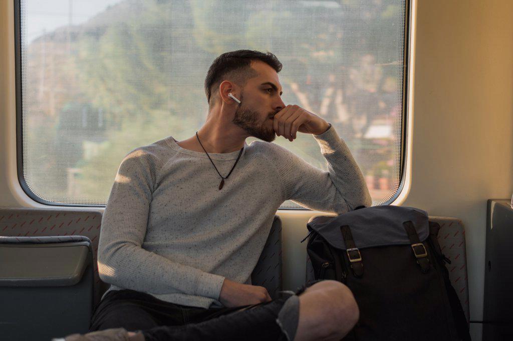 THOUGHTFUL YOUNG MALE PASSENGER LISTENING TO MUSIC IN SUBWAY CAR