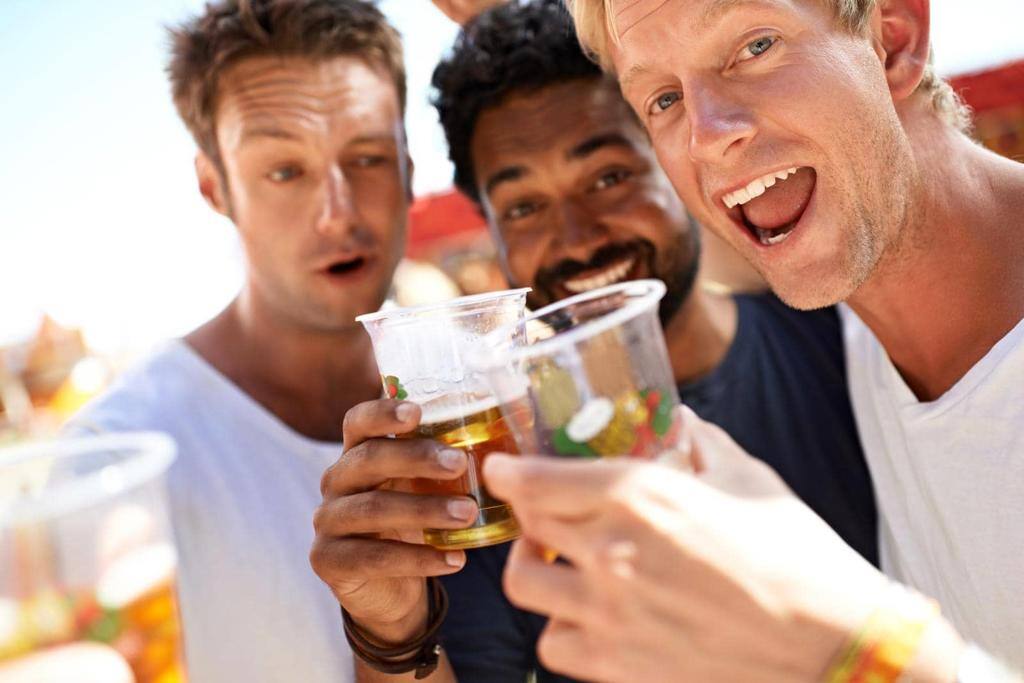 THREE YOUNG MEN TOASTING THEIR BEERS AT A MUSIC FESTIVAL