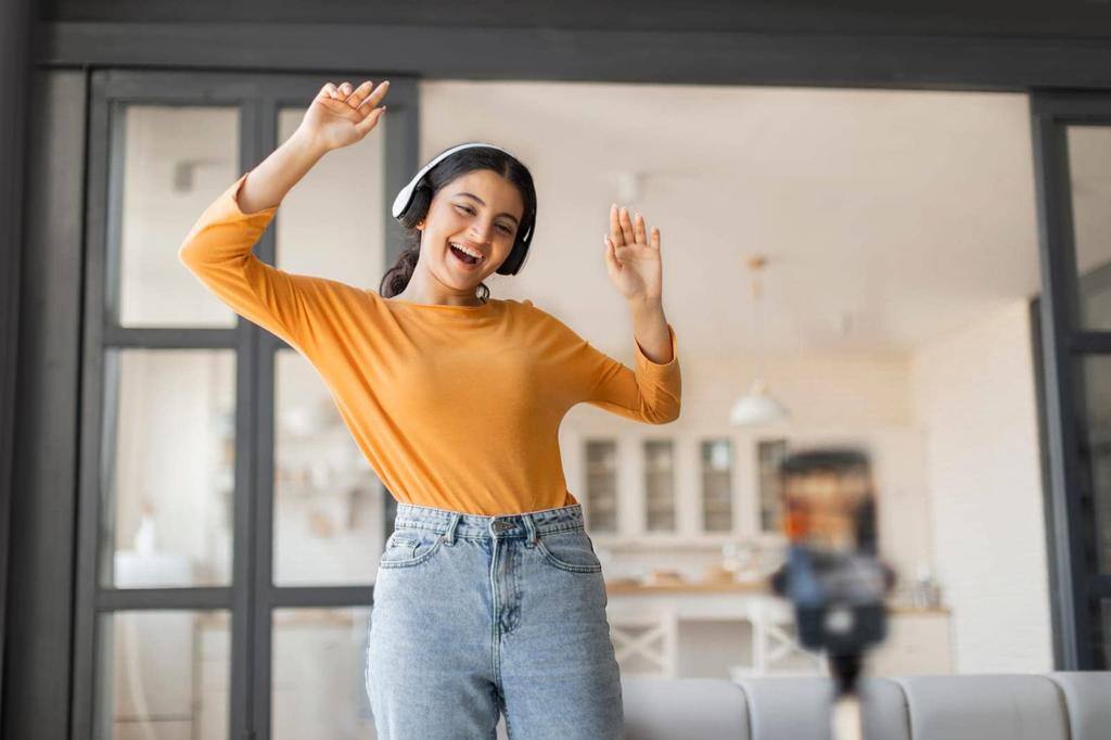 Cheerful young indian vlogger with headphones dancing joyfully while recording video