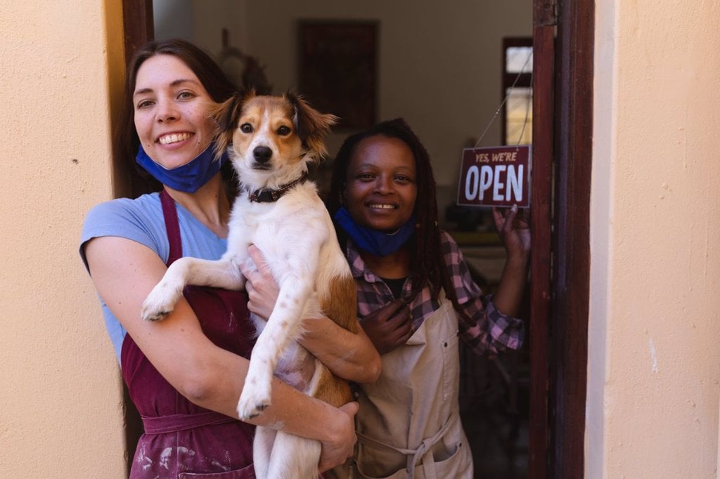 PORTRAIT OF CAUCASIAN AND MIXED RACE WOMEN AT POTTERY STUDIO, HOLDING A PUPPY