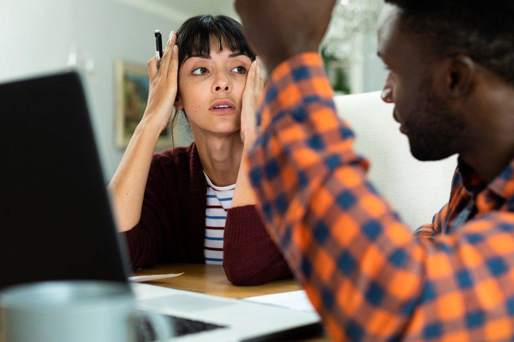 TENSED MULTIRACIAL YOUNG COUPLE DISCUSSING HOUSEHOLD BUDGET AT HOME